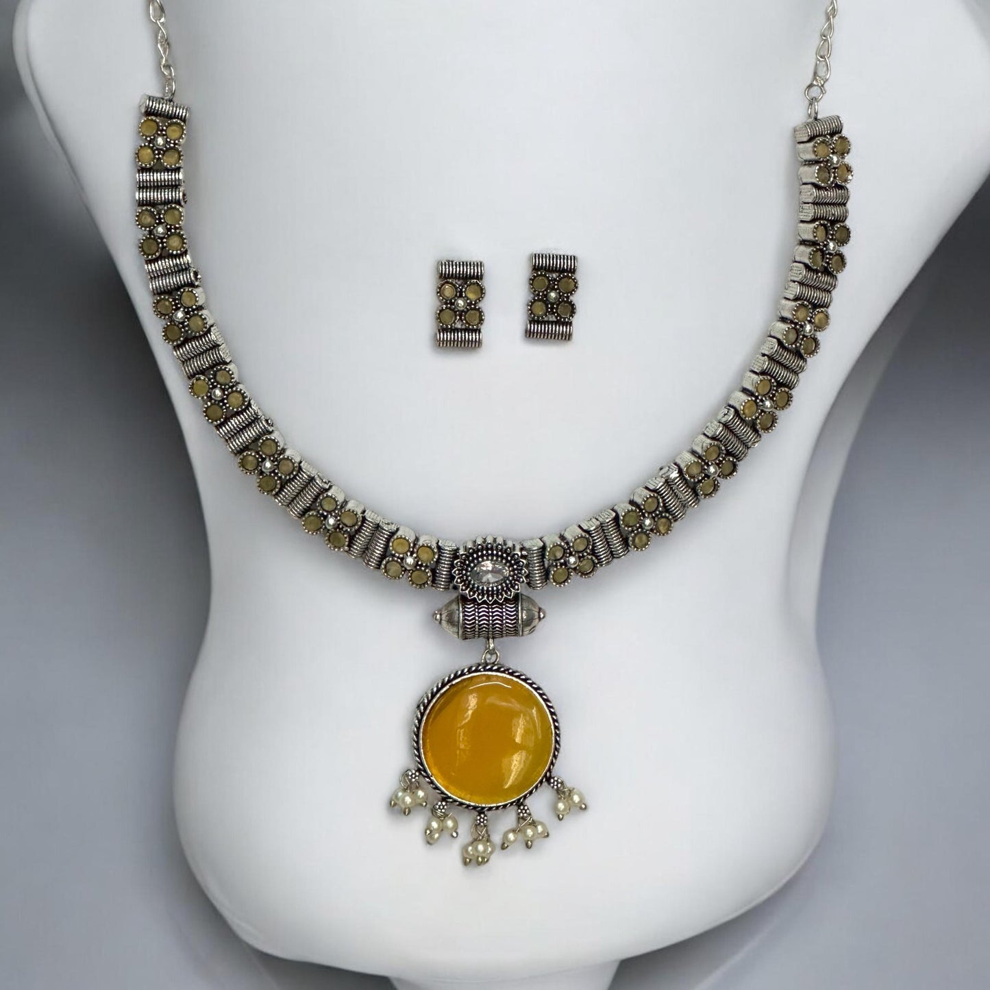 Silver look alike oxidised necklace set in yellow with circular pendant, pearl drops, and matching earrings displayed on white bust stand