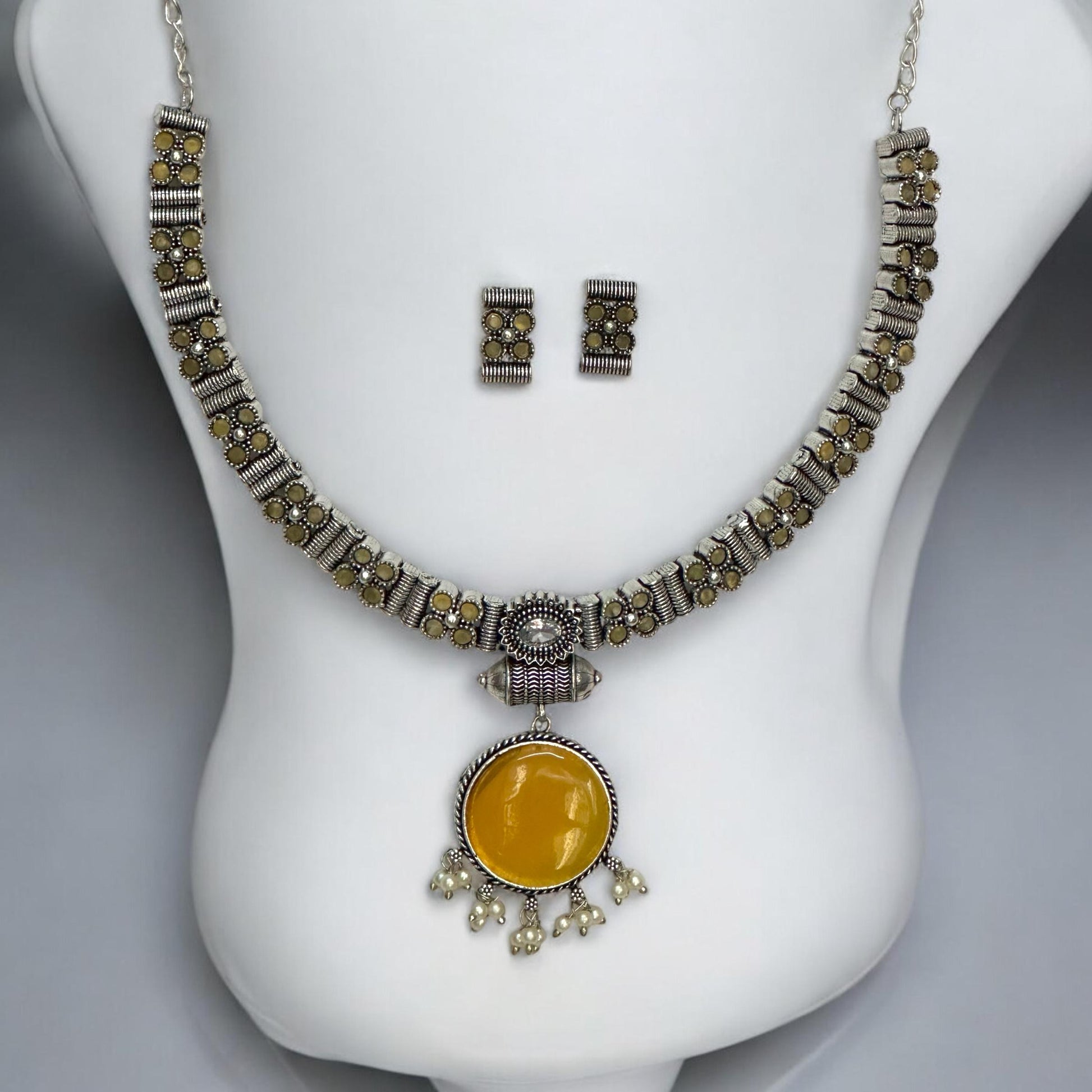 Silver look alike oxidised necklace set in yellow with circular pendant, pearl drops, and matching earrings displayed on white bust stand