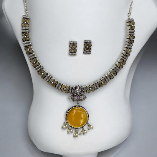 Silver look alike oxidised necklace set in yellow with circular pendant, pearl drops, and matching earrings displayed on white bust stand