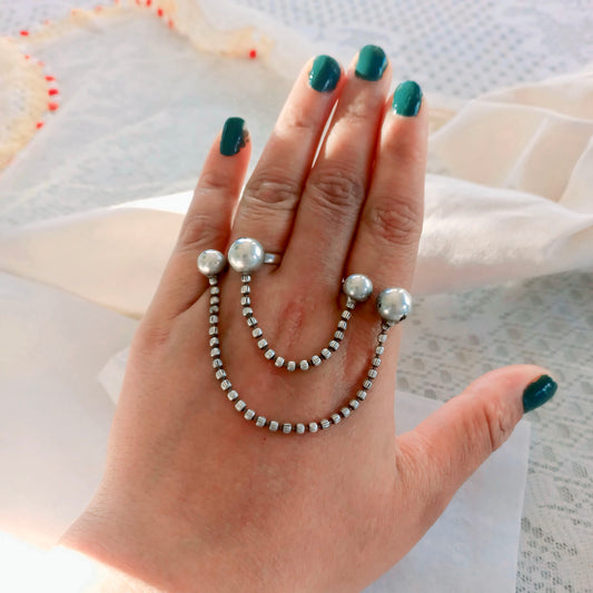 A woman's hand adorned with a Silver Replica Adjustable Double Finger Ring, featuring silver-toned chain links and pearl-like accents draped across two fingers, creating a bold fashion statement.