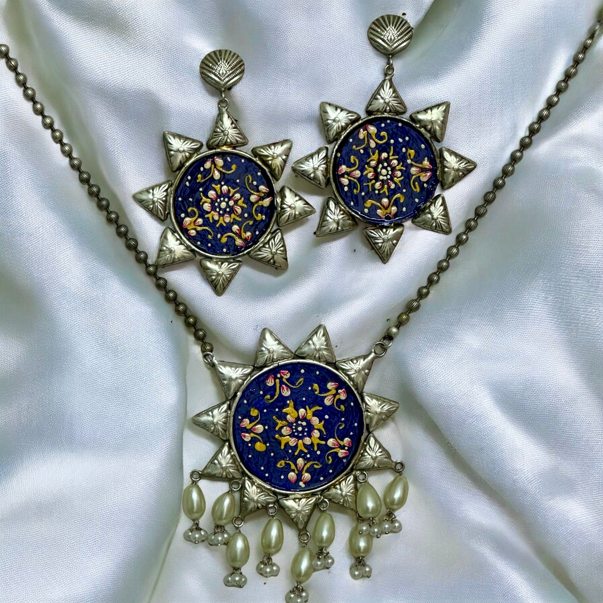 Oxidized silver replica necklace with large blue floral pendant and matching earrings on white fabric – Bella & Diva