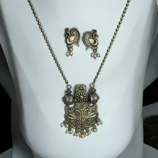 Silver replica designer chain pendant set in antique peacock design with pearl drops and matching earrings displayed on white jewellery stand