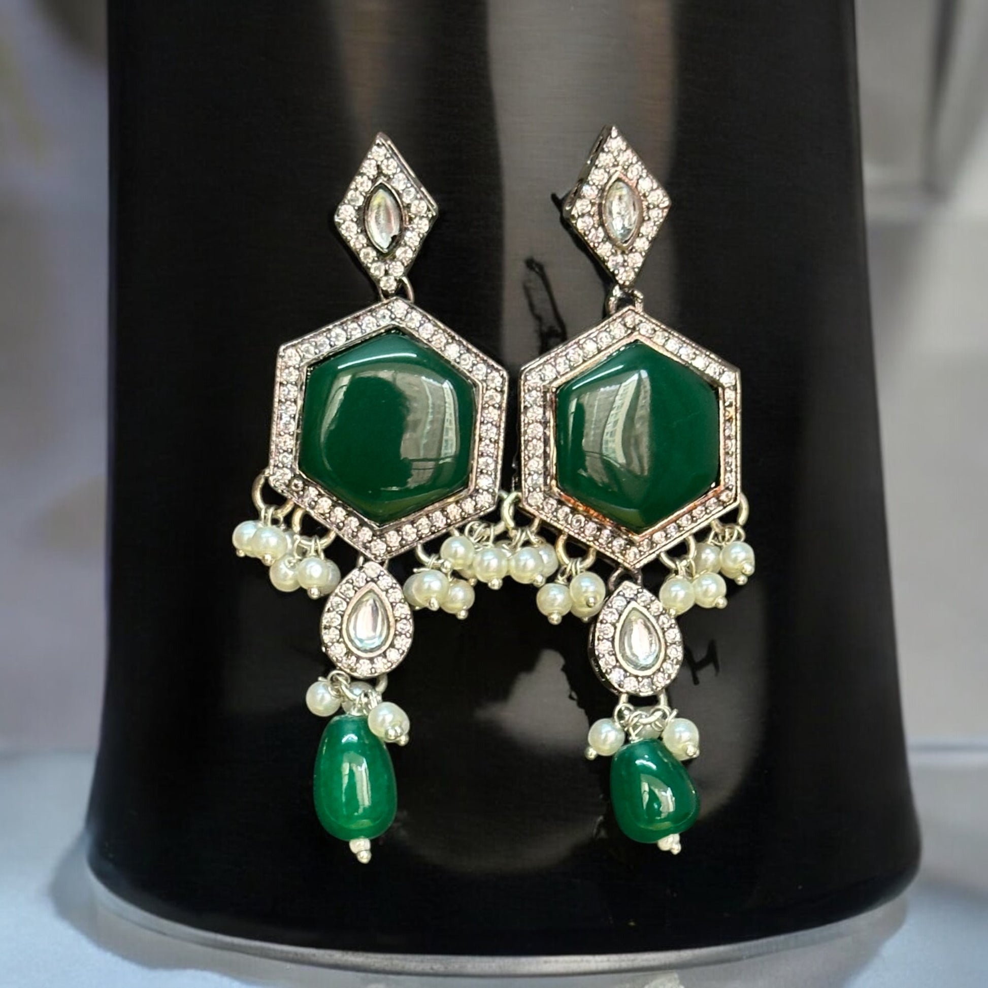 Silver-look alike Earrings with green Monalisa stones and intricate diamond work, featuring a statement floral pendant with pearl and bead danglers, displayed on a black jewelry bust with a soft light background.