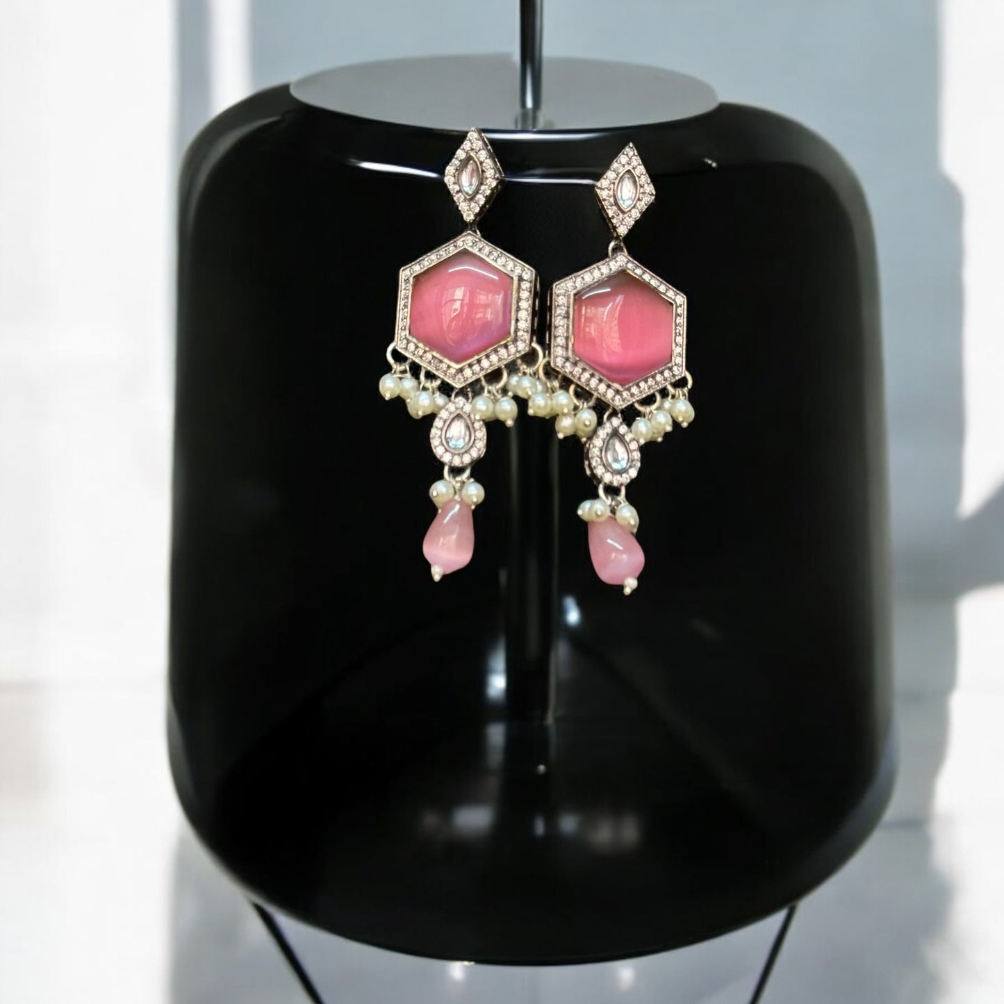 Silver Look-Alike Earrings of a set adorned with pink Monalisa stones and intricate diamond work. The earrings are displayed against a black coloured jewellery display stand with a shine and a light white background. 