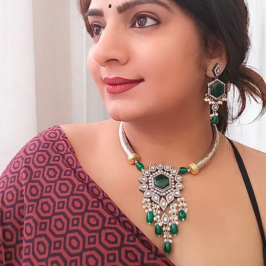 A Model displaying Silver-look alike Hasli necklace adorned with green Monalisa stones and intricate diamond work, featuring a statement floral pendant with pearl and bead danglers, paired with matching green stone earrings.