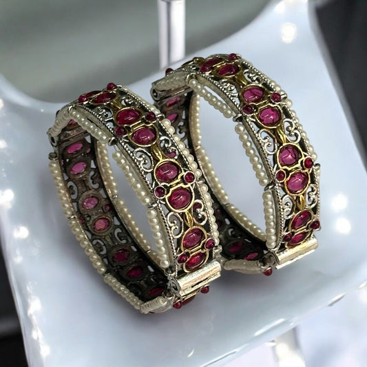 Elegant silver replica bangles with intricate ruby stone detailing and pearl accents placed on a white coloured jewellery display stand.