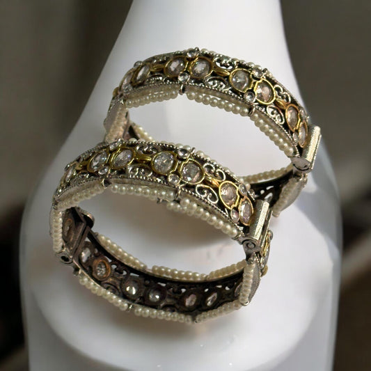 Elegant silver replica bangles adorned with intricate white pearl detailing and sparkling stonework. It is standing on a white coloured jewellery display stand.
