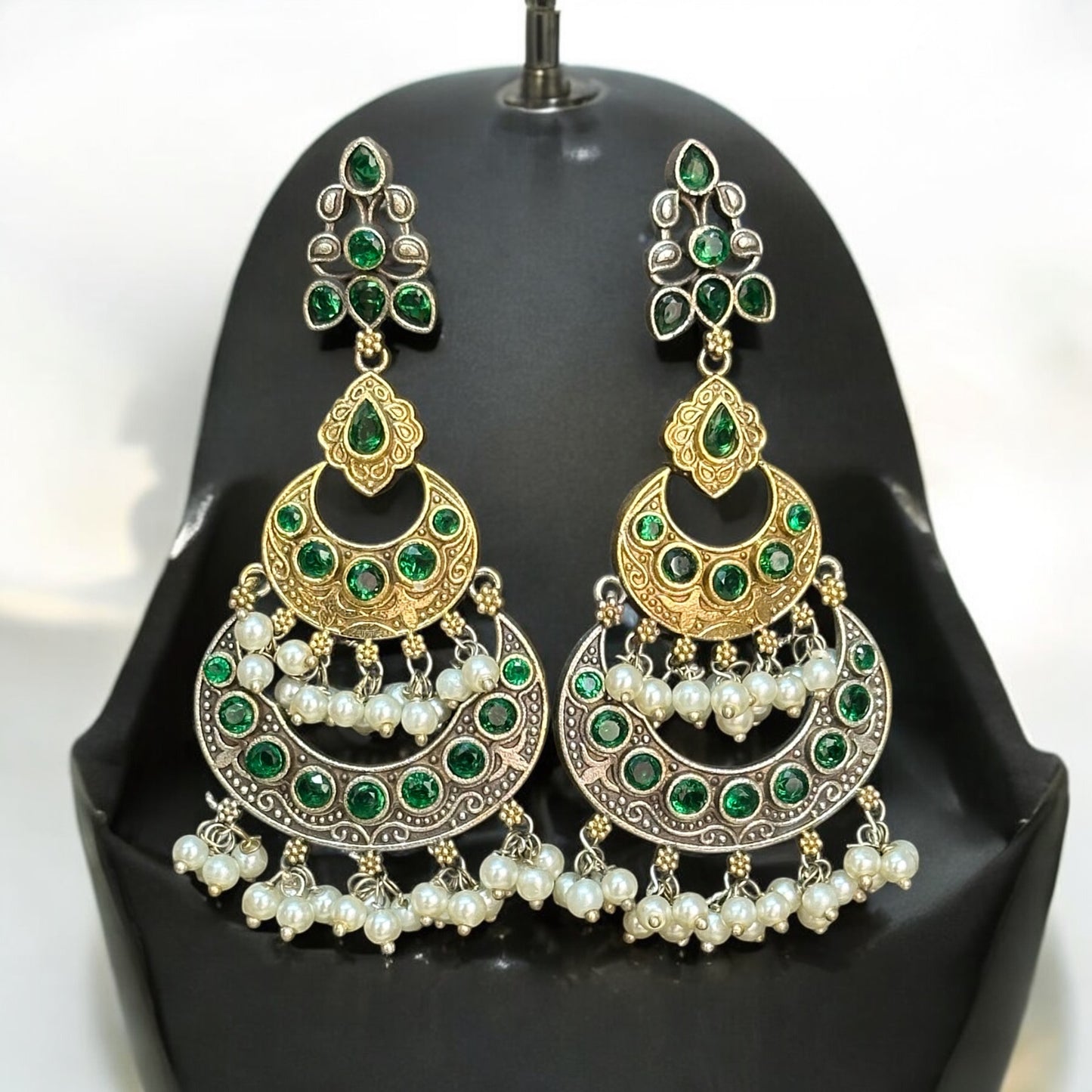Silver replica Earrings with a round green and gold toned design, adorned with pearl danglers, paired with large green and gold jhumka-style featuring intricate detailing, displayed on a black jewelry bust against a soft-lit background.
