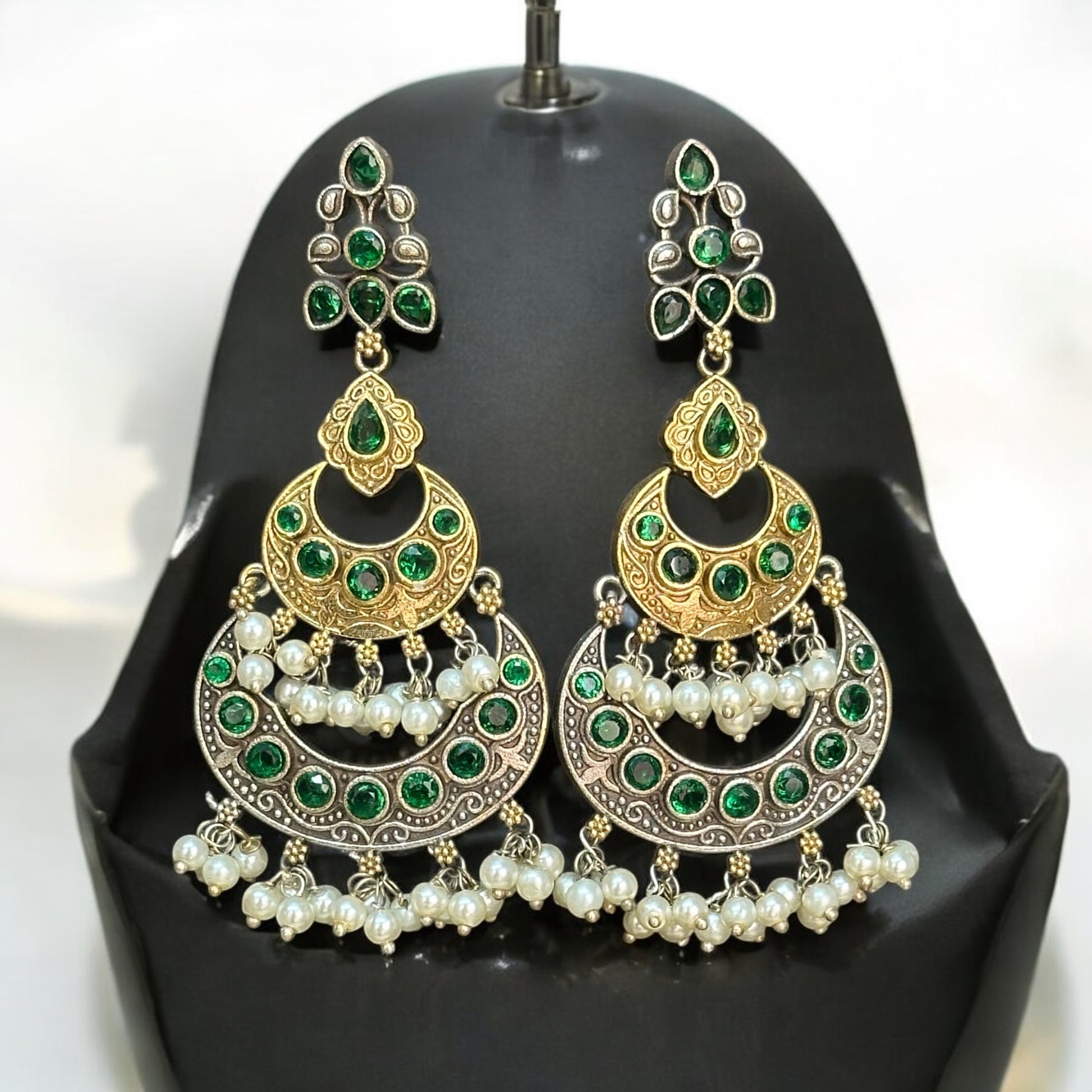 Silver replica Earrings with a round green and gold toned design, adorned with pearl danglers, paired with large green and gold jhumka-style featuring intricate detailing, displayed on a black jewelry bust against a soft-lit background.