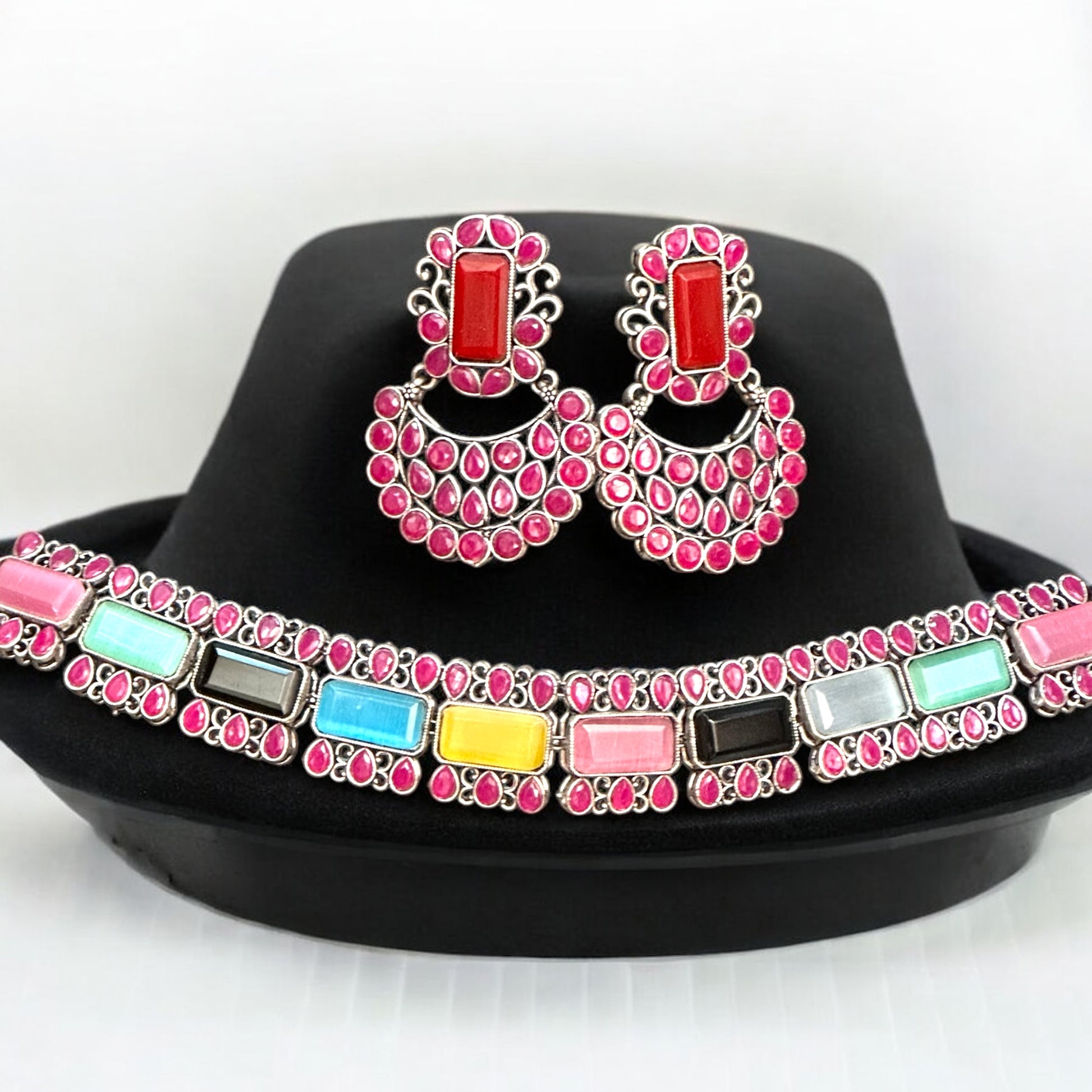 Silver Replica Multicolour Choker Necklace featuring vibrant gemstones in pink, blue, yellow, and more, paired with matching Chandbali-style earrings, displayed on a black velvet stand.
