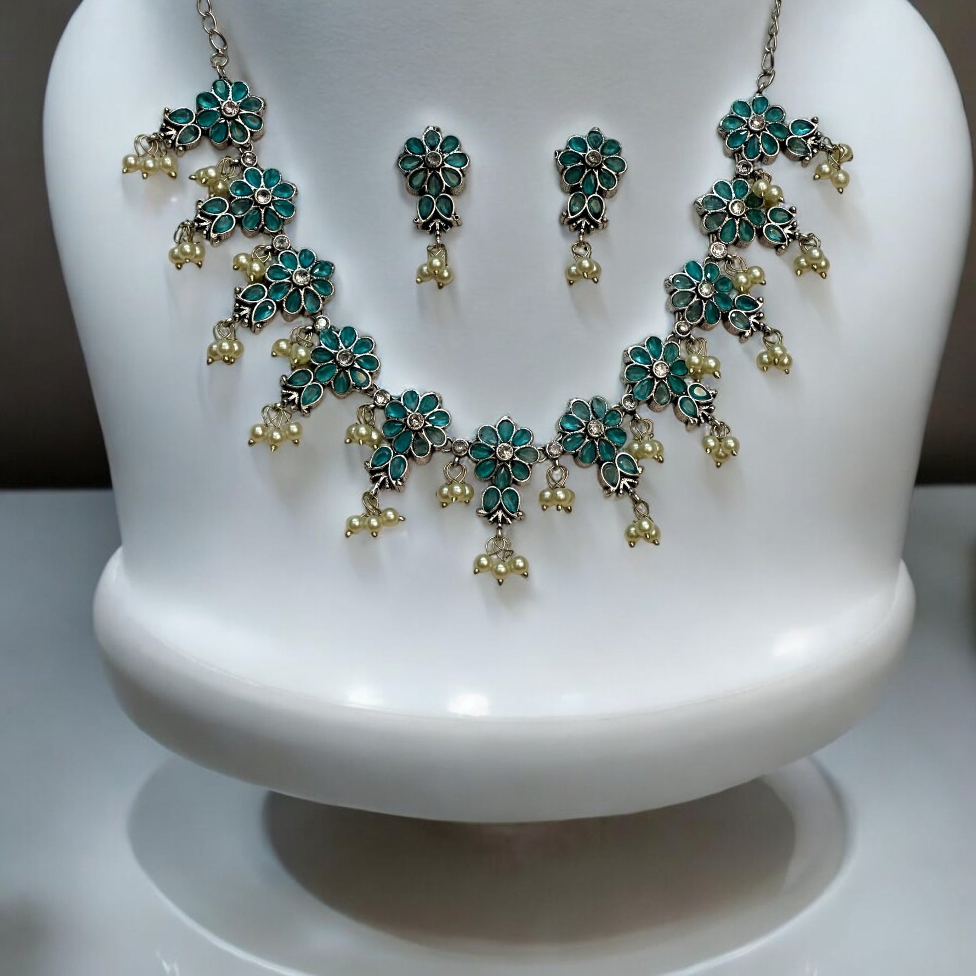 Silver Replica Necklace Set in Sky Blue featuring delicate floral motifs adorned with pearl accents, paired with matching earrings, displayed on a white mannequin stand.