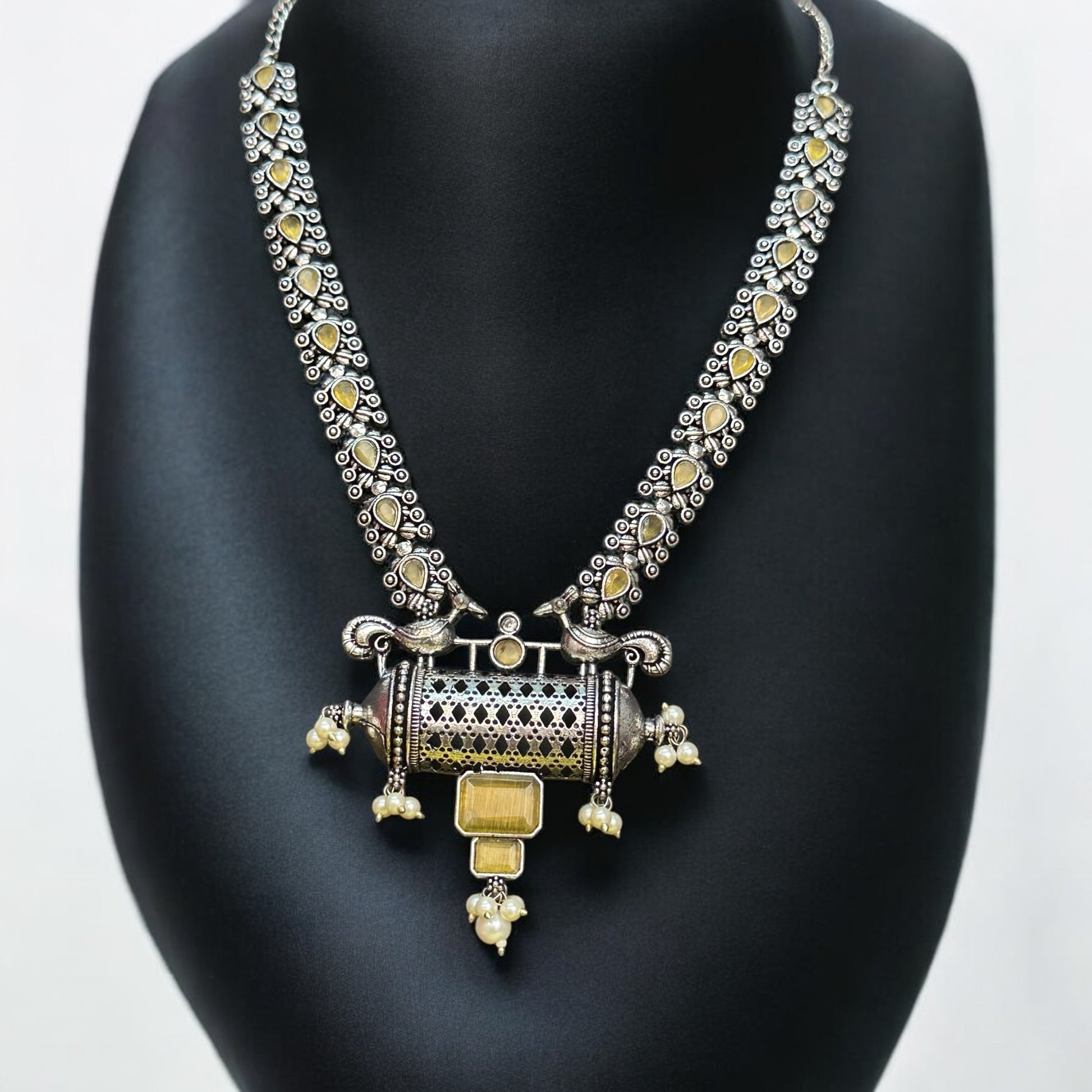 Silver Replica Necklace Set with intricate detailing and yellow accents, displayed on a black mannequin, featuring a statement cylindrical pendant with pearl and gold embellishments.