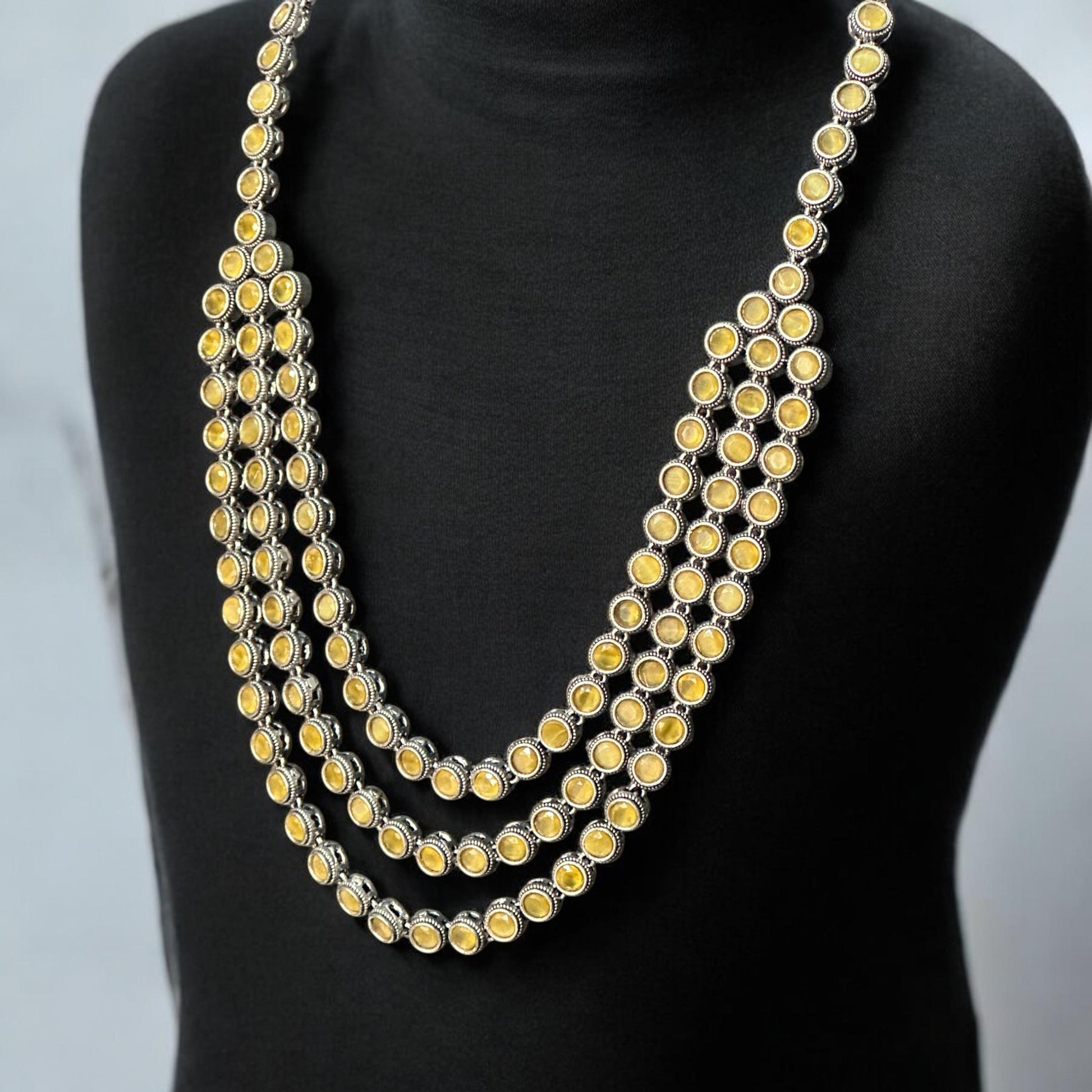 Silver replica three-layer necklace set with yellow stones displayed on black mannequin bust