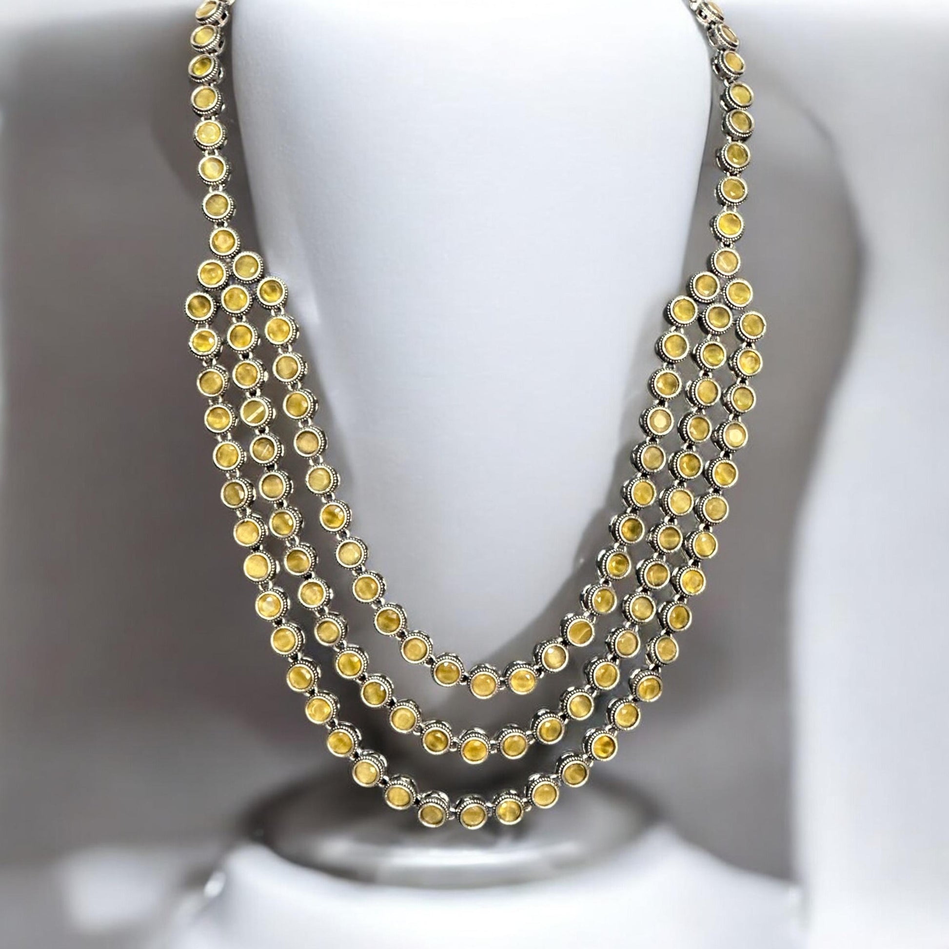 Silver replica three-layer necklace set with yellow stones displayed on white mannequin bust