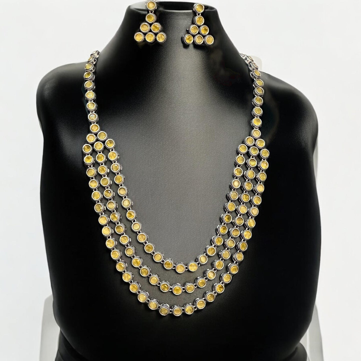Silver replica three-layer necklace set with yellow stones and matching triangle earrings displayed on black mannequin bust