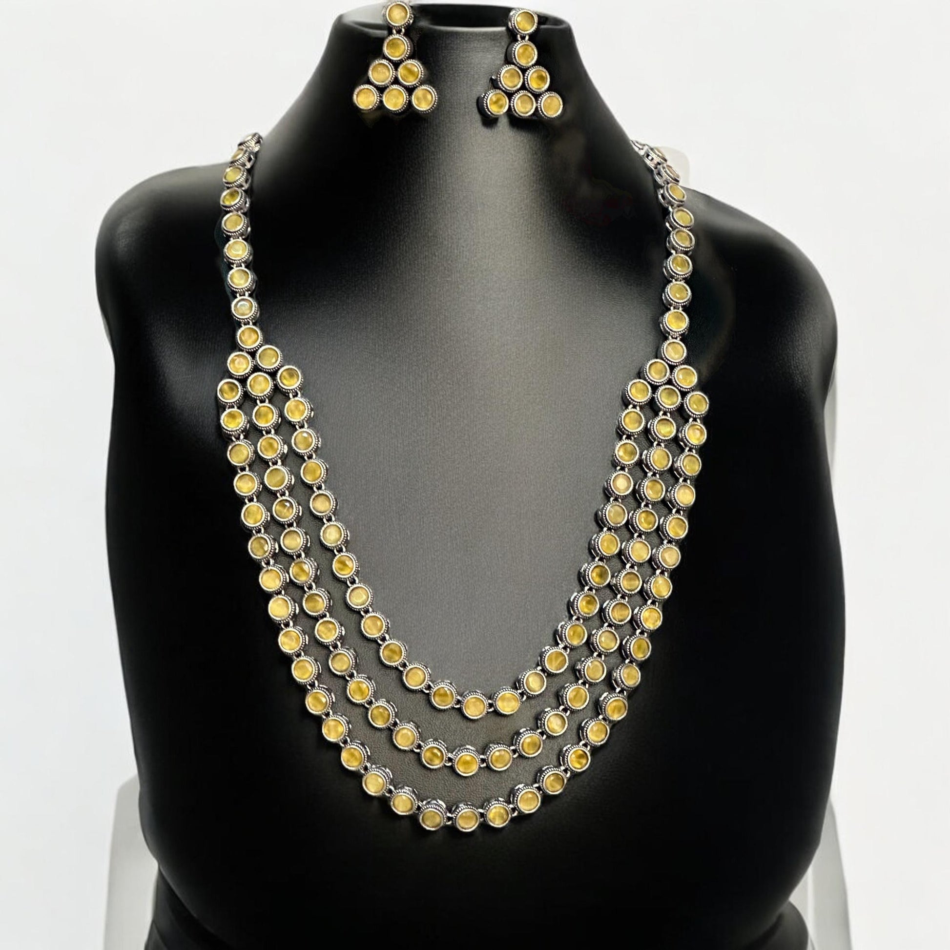 Silver replica three-layer necklace set with yellow stones and matching triangle earrings displayed on black mannequin bust