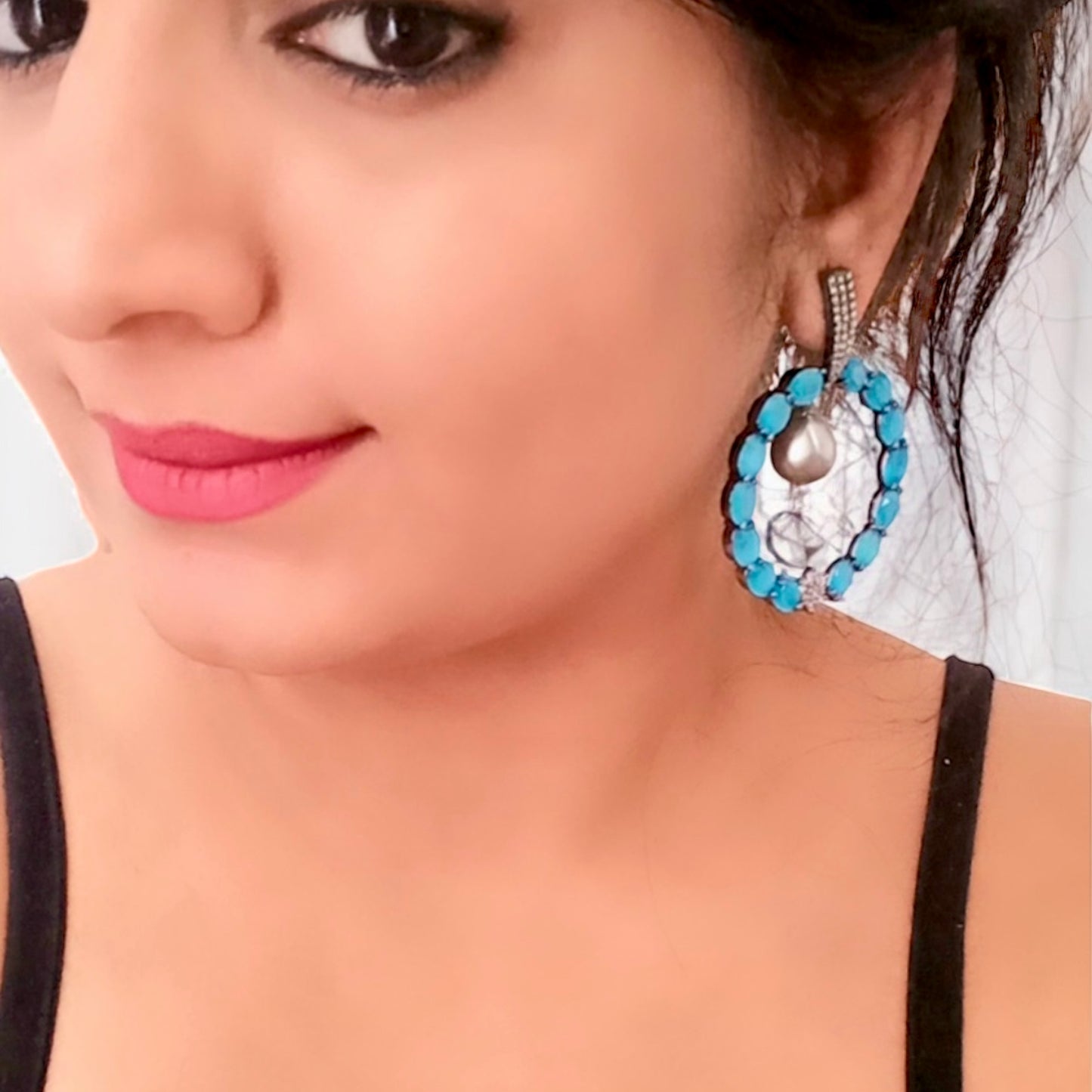 A Model displaying a Statement American diamond earrings featuring a circular blue stone design with a hanging pearl drop, perfect for partywear. 