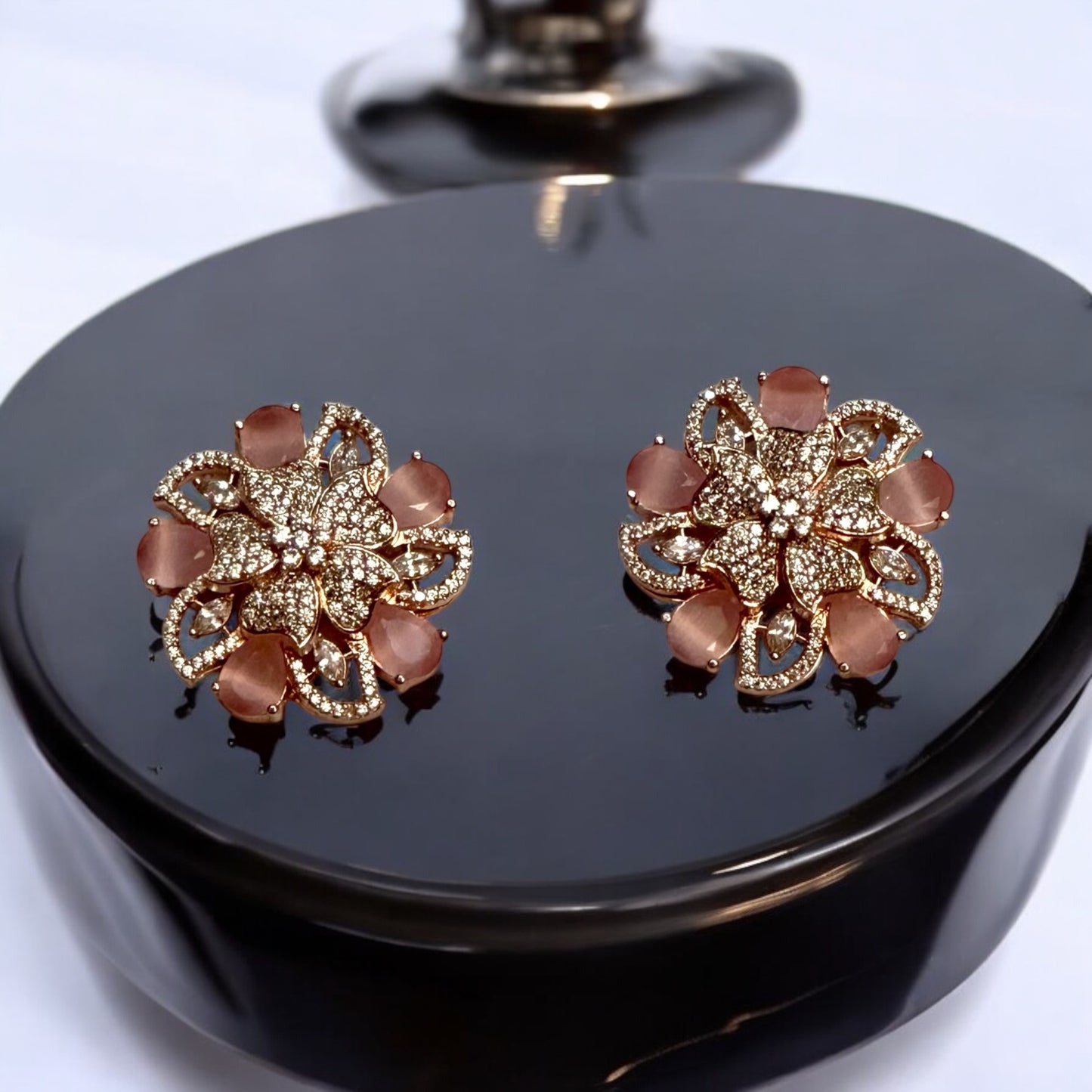 Statement rose gold polish earrings with American diamonds and peach-hued floral accents placed on a black coloured jewellery display stand.