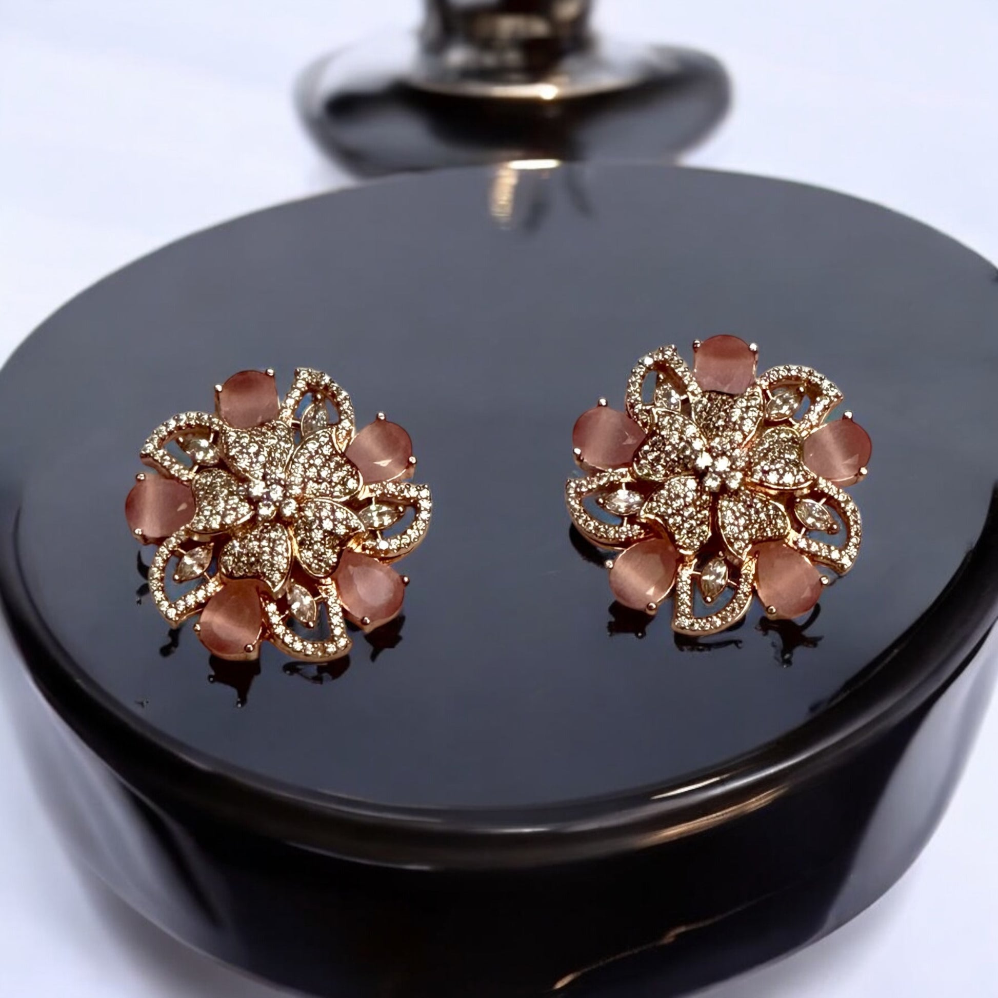 Statement rose gold polish earrings with American diamonds and peach-hued floral accents placed on a black coloured jewellery display stand.
