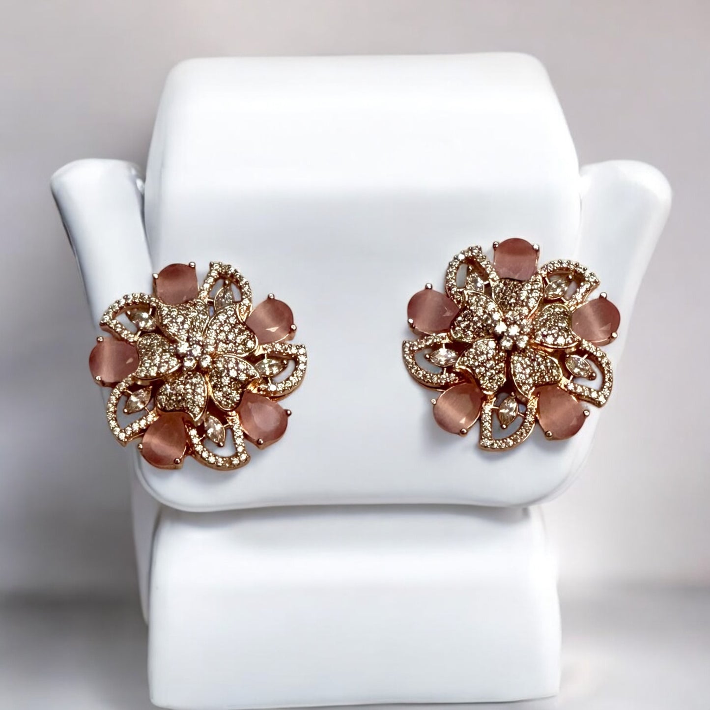 Statement rose gold polish earrings with American diamonds and peach-hued floral accents placed on a white jewellery display stand.