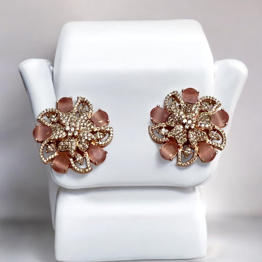 Statement rose gold polish earrings with American diamonds and peach-hued floral accents placed on a white jewellery display stand.