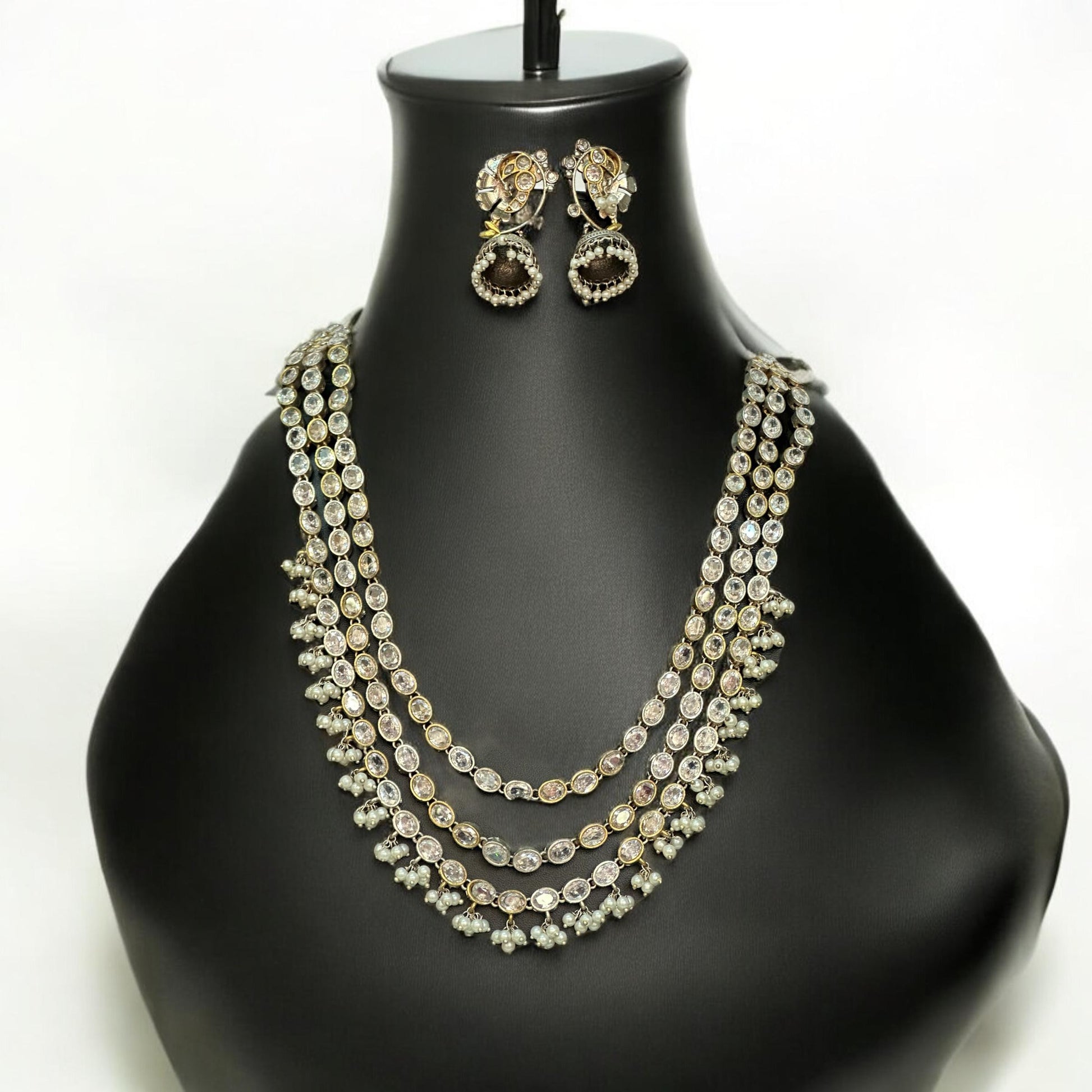 Statement silver replica necklace set featuring three layers of dazzling white stones with matching jhumka earrings, displayed on a black mannequin with intricate detailing.