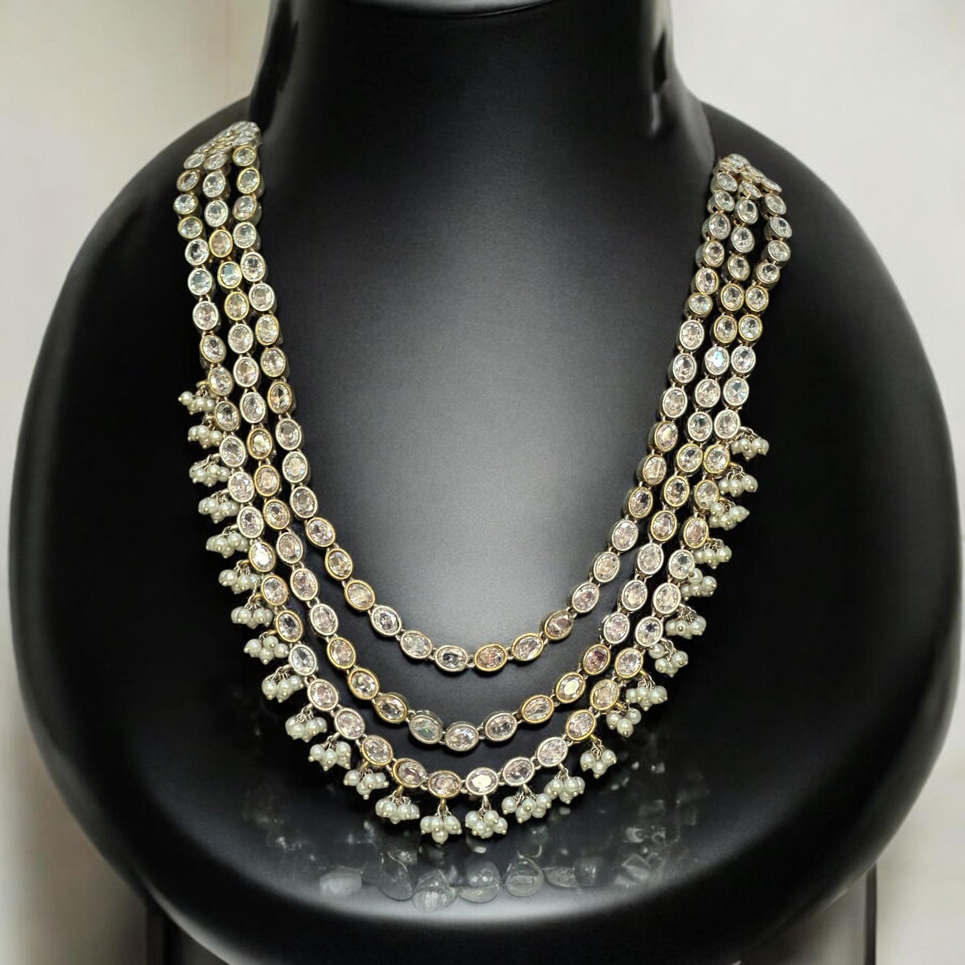 Statement silver replica necklace featuring three layers of dazzling white stones, displayed on a black mannequin with intricate detailing.