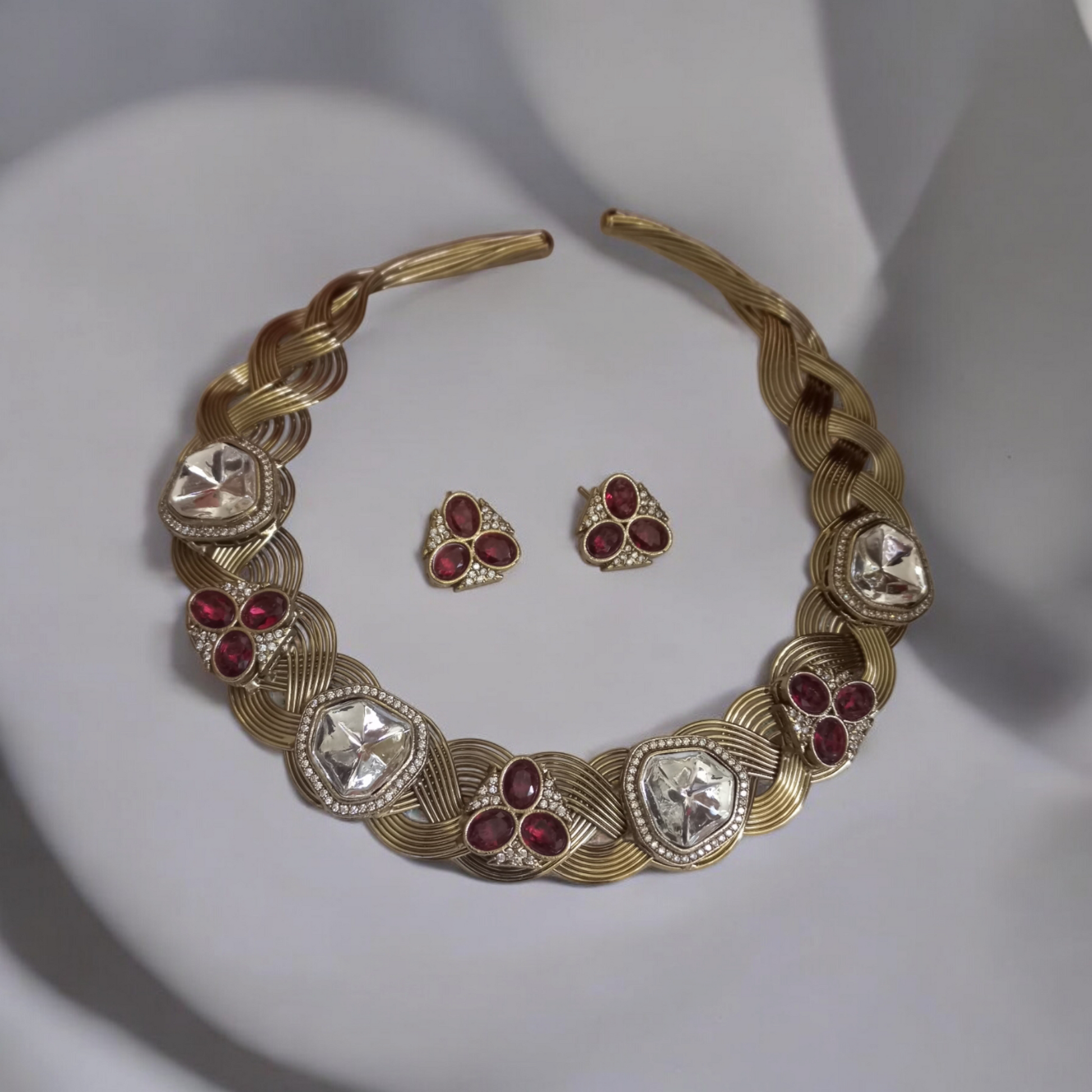Statement hasli necklace with Apala polish in gold and ruby tones, featuring moissanite stones and matching earrings, laid against a neutral backdrop.
