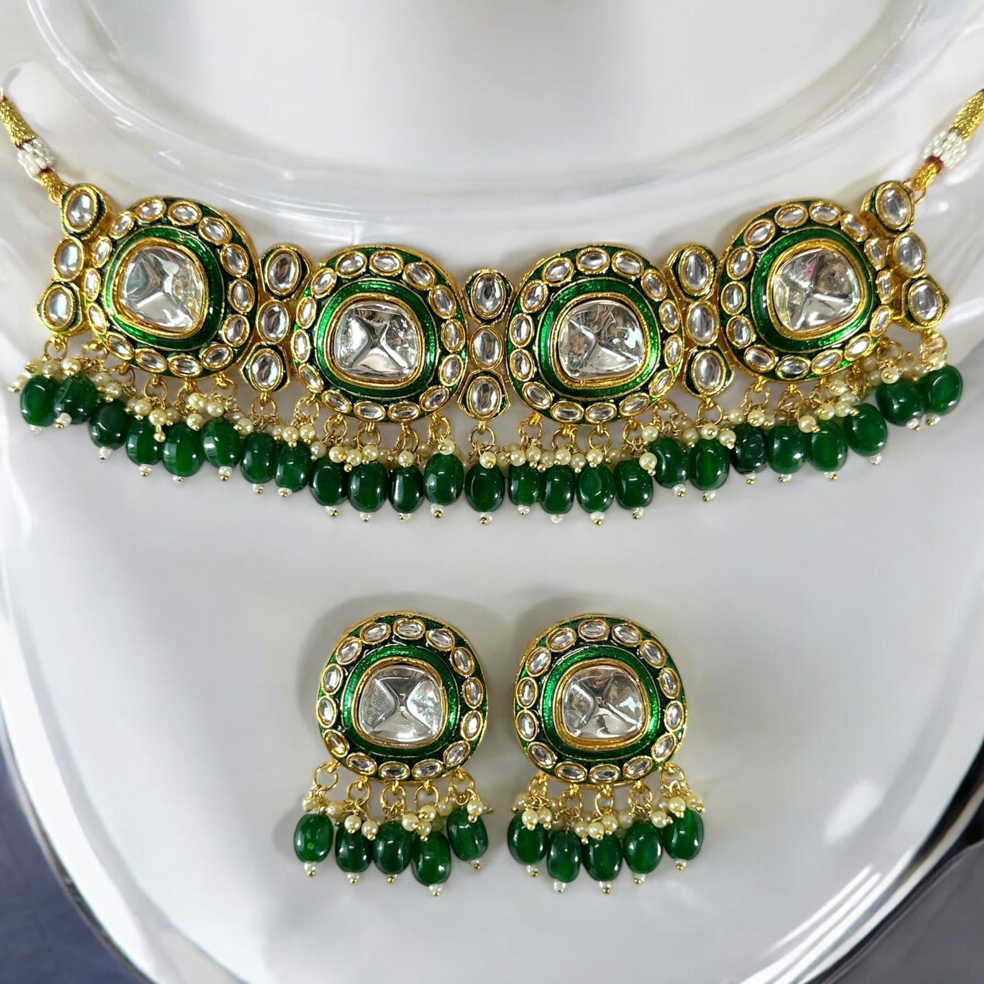 polki kundan statement choker necklace and earrings In Green placed on a white colored jewellery display stand.