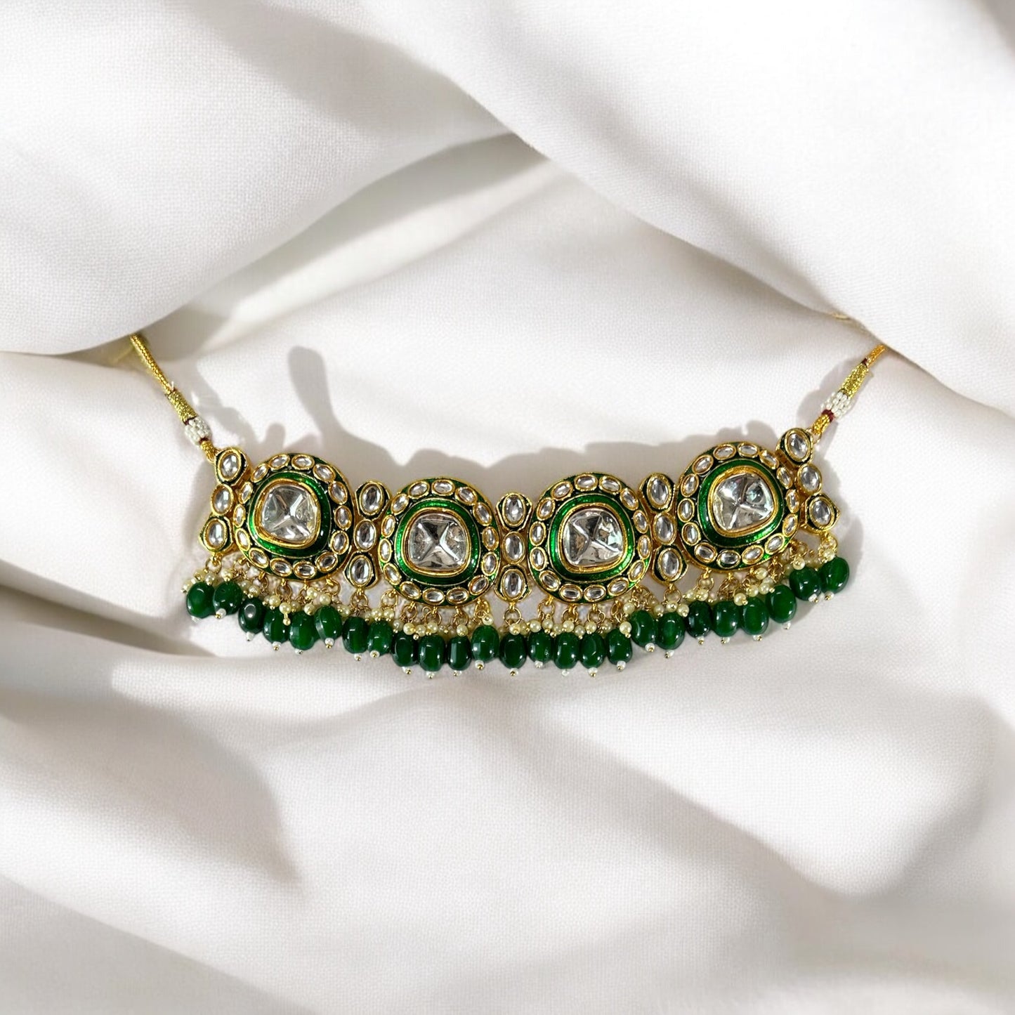 polki kundan statement choker necklace In Green placed on a white colored fabric.