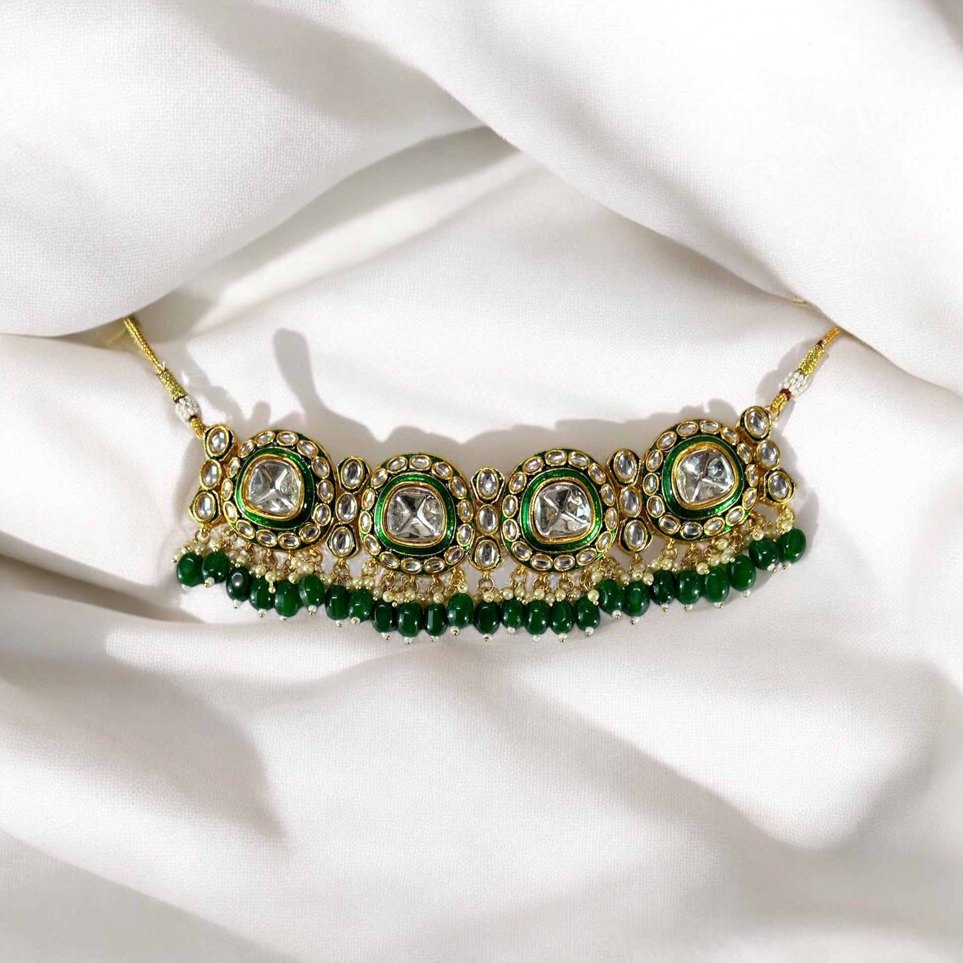 polki kundan statement choker necklace In Green placed on a white colored fabric.