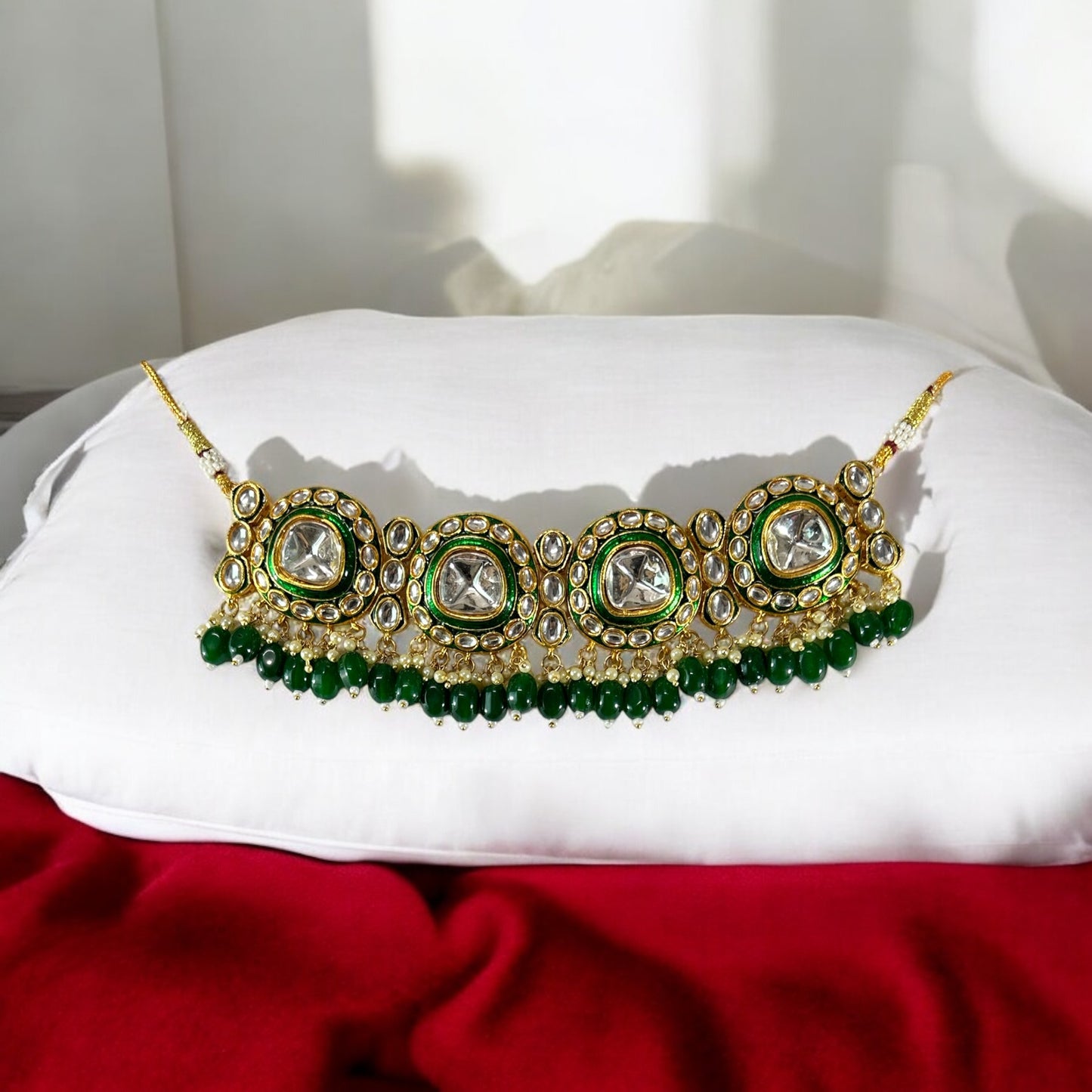 polki kundan statement choker necklace In Green placed on a white and red colored fabric.stand.
