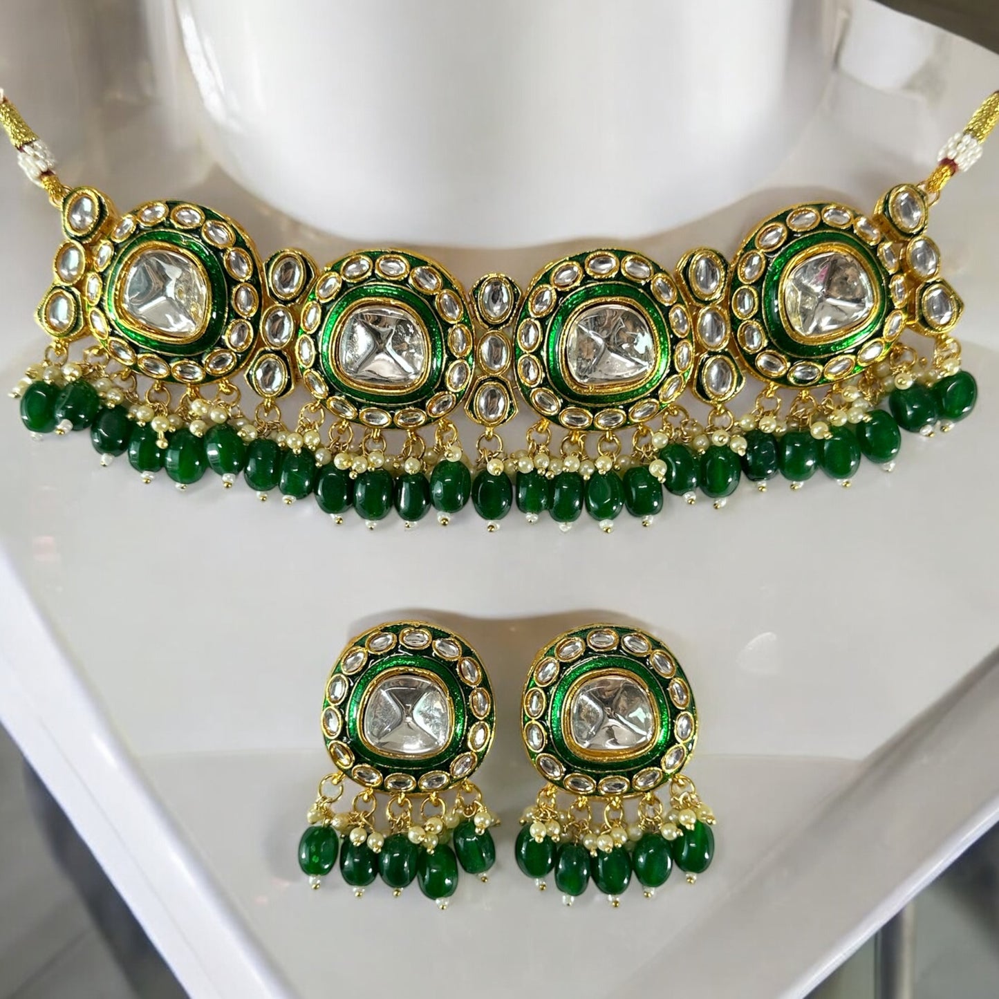 polki kundan statement choker necklace set In Green placed on a white coloured jewellery display stand.